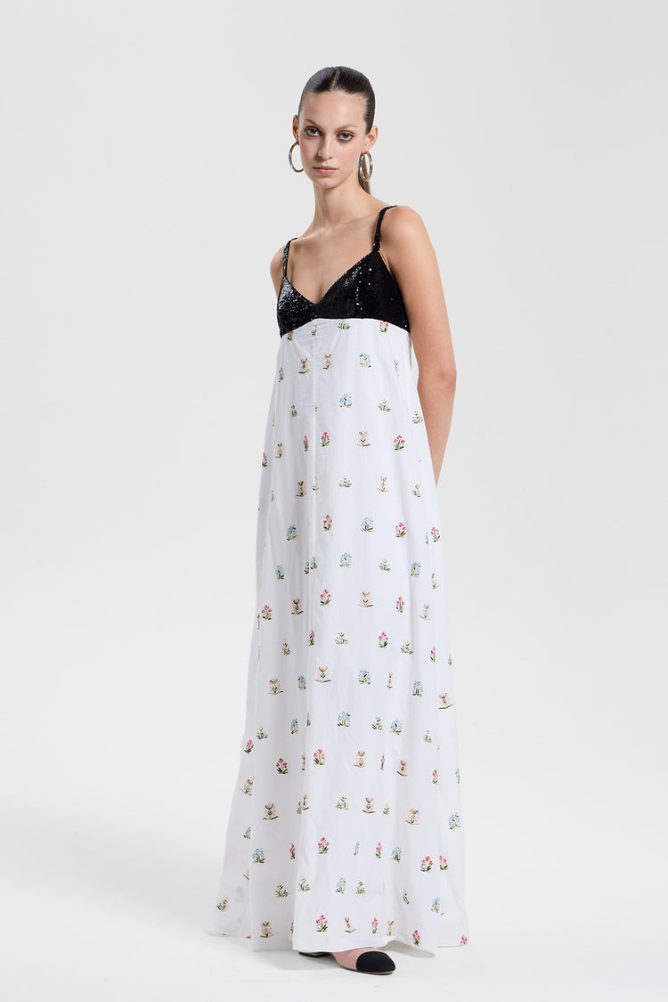 Woman wearing a white dress with floral pattern and black sequin top on a white background