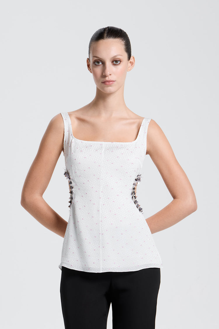 Woman wearing a white polkadot sleeveless top with sequin embellishments on a light gray background